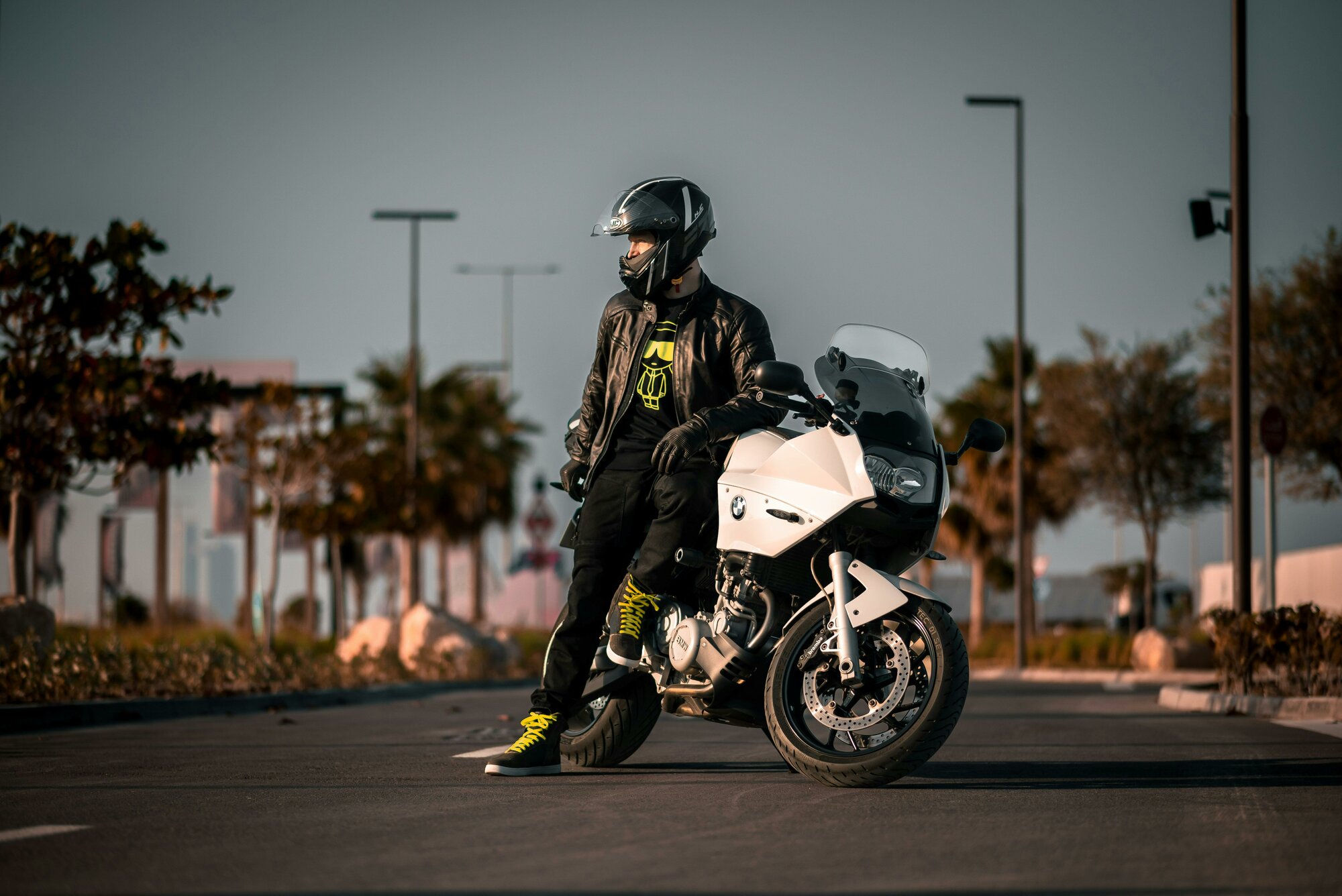 Muž stojí pri motorke bielej farbe a na hlave má čiernu prilbu pre motorkára.