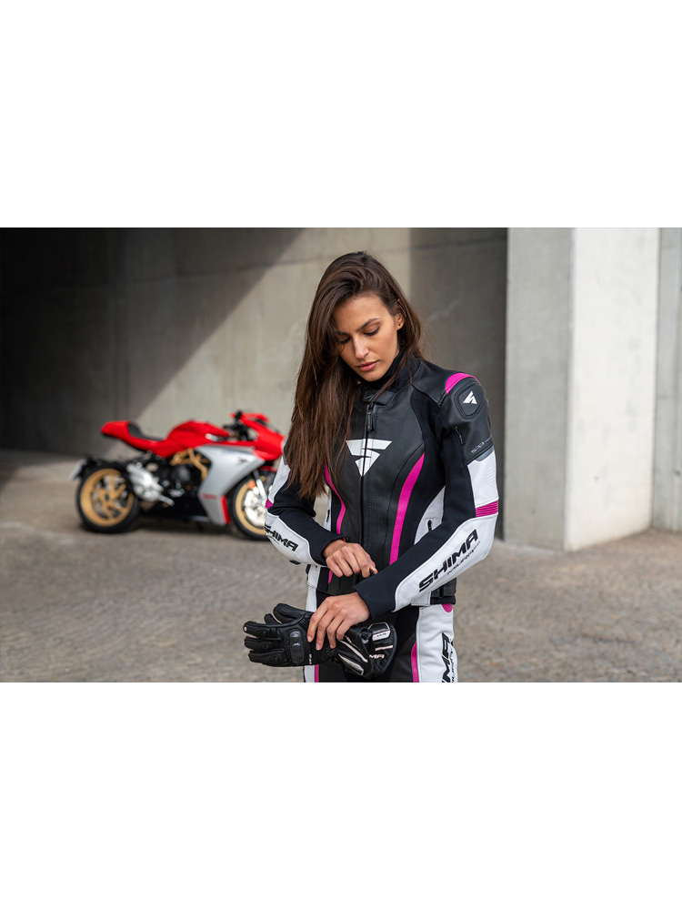 Žena má na sebe kombinézu na motorku a v ruke rukavice na motorku